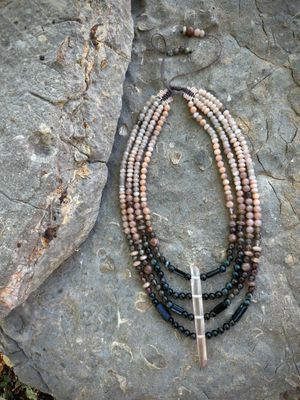 A necklace of black, deep, blue and dusty, pink, semi precious stone beads lays on a fossil filled stone