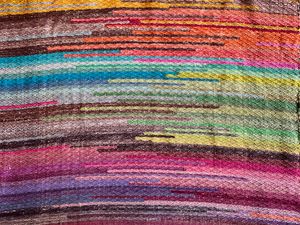 A hand woven piece of fabric with rays and stripes in rainbow colors