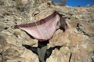 A woman stands in front of a cliff with a pink naturally dyed scarf