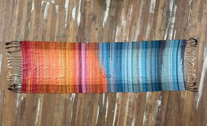 A handwoven shawl, half the colors of fire and half the colors of ice lays on a wooden floor