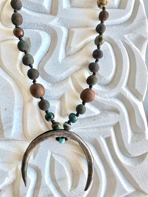 a necklace with a silver crescent moon and clay beads on a white marble sculpture