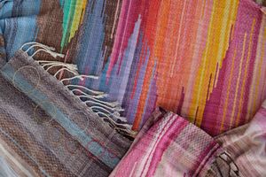 A length of handwoven fabric in earth hues as well as rainbow and sunrise colors lays on a wooden floor