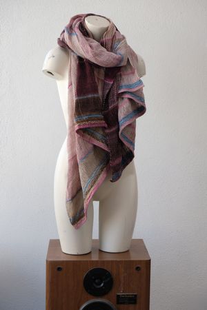 A handwoven scarf shawl loosely woven in earthy pinks and indigo blue rests on a white mannequin