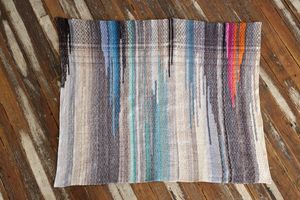 a rectangle piece of handover fabric in blues, gray pink and orange dress on a wooden floor