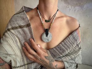 A woman wearing a naturally dyed shawl and tattooed hand wears a stone necklace