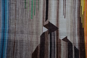 A detail of the geometric tapestry woven designs on a shawl in grayscale, earth-tones and elemental colors