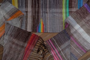 A detail of a length of handwoven fabric in earth-tones and all the colors of the rainbow in prismatic sequence
