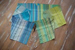 on an oak wood floor is laid 5 meters of handwoven fabric in textured stripes of greens on one side and shades of blue on the other